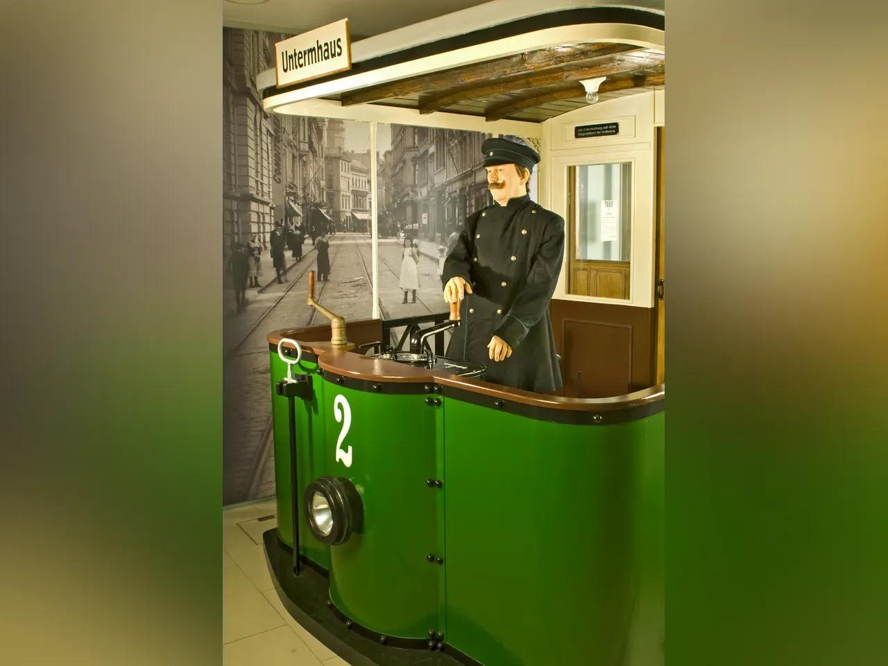 Ausstellungsinszenierung mit einer Straßenbahn um 1900 und Straßenbahnfahrer. Im Hintergrund ist die Schlossstraße mit Straßenbahnschienen zu sehen und eine Werbetafel mit verschiedenen Anzeigen
