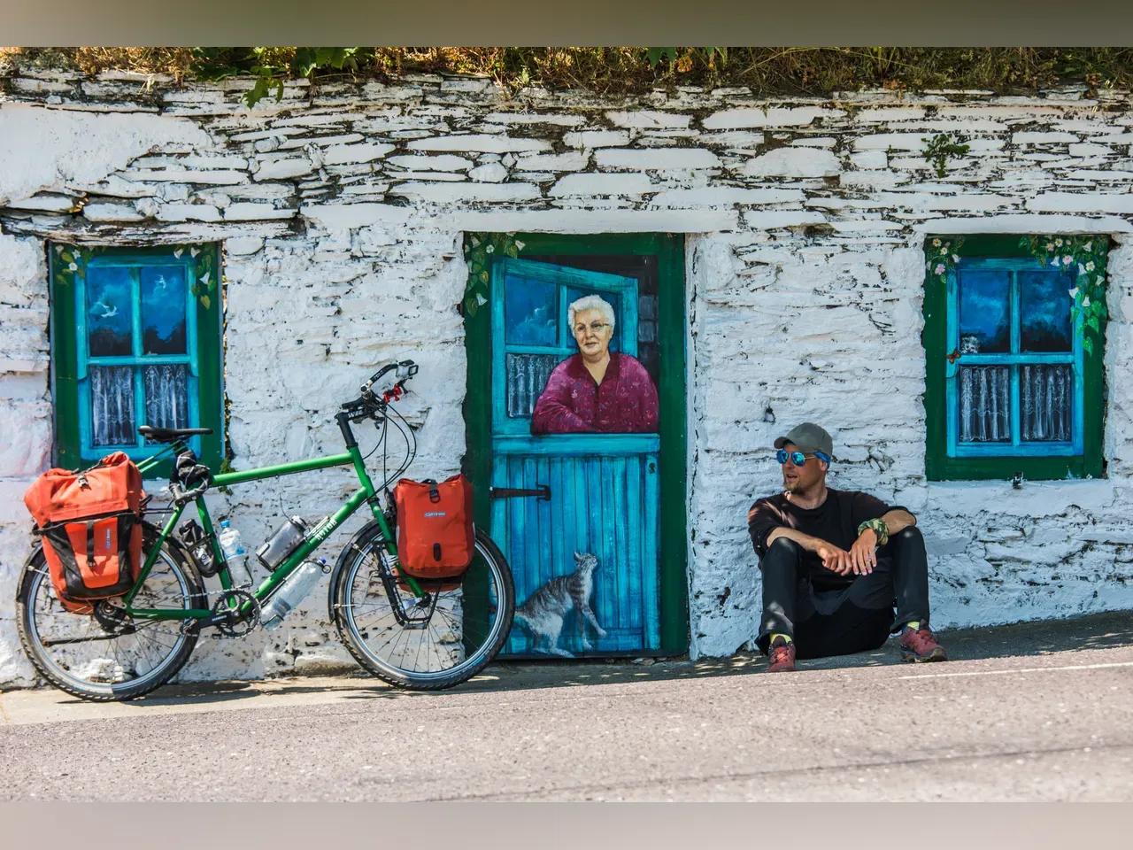 Robert Neu mit seinem Fahrrad vor einem bunt bemalten Haus in Irland