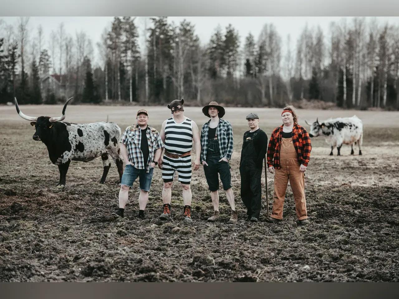 Die 5 Musiker:innen auf einem Feld mit 2 Kühen