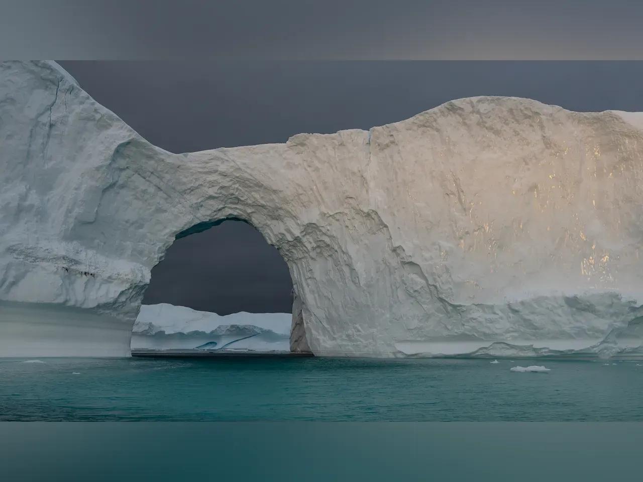 Eine Eismasse im Wasser von Grönland mit einem naturgeschaffenen Torbogen.