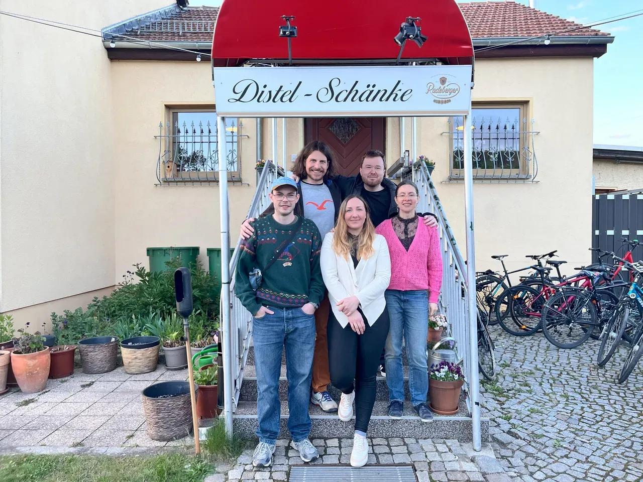 5 Personen stehen vor den Treppen der Distel-Schänke und blicken fröhlich in die Kamera.