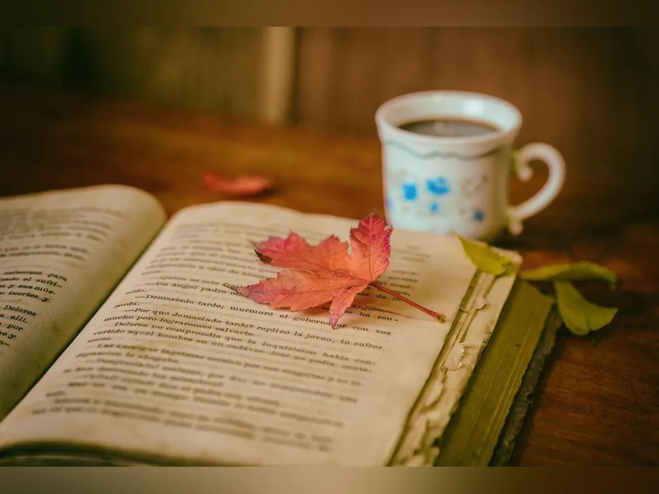Herbstlich-atmosphärisches Bild mit einer Kaffeetasse und einem aufgeschlagenem Buch, auf dem ein Blatt liegt